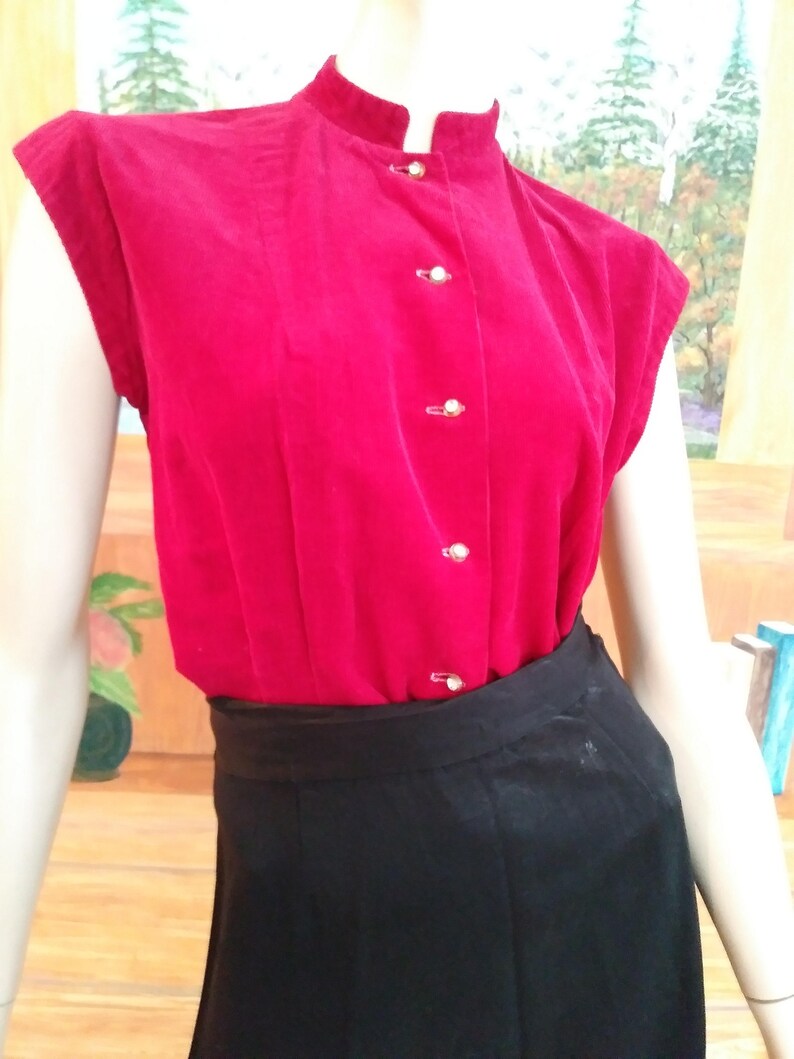 May include: A red sleeveless blouse with a mandarin collar and gold buttons. The blouse is made of a soft, textured fabric.
