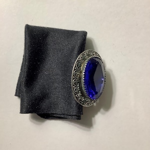 May include: A silver ring with a large, dark blue gemstone set in a decorative, ornate frame.