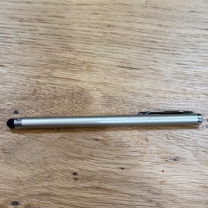 May include: A slim, cylindrical stylus with a metallic silver finish, featuring a black rubberized tip at one end and a silver-colored metal pocket clip attached to the opposite end, designed for use with touch-sensitive electronic screens.