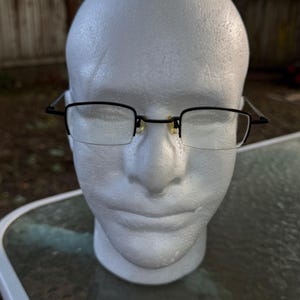 May include: Rectangular eyeglasses featuring a thin black metal frame and clear lenses. The glasses have a semi-rimless design where the black metal only outlines the top of the lenses, while the bottom edges are rimless. Includes adjustable nose pads.