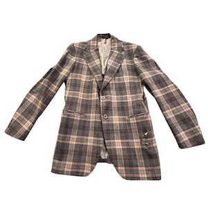 May include: A gray plaid blazer with a two-button closure, featuring a classic notched lapel and two front pockets. The jacket has a light tan and dark gray plaid pattern. The blazer has a distressed detail on the lower right side.
