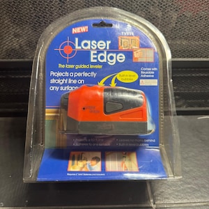 Puede incluir: Un nuevo nivel láser Laser Edge en su embalaje original. El nivelador es rojo y negro, con las palabras "Laser Edge" impresas en el lateral. El embalaje es azul y blanco, con las características del producto.