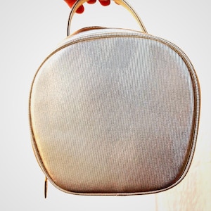 May include: Silver-toned, oval-shaped vintage handbag with a handle. The bag features a vertically ribbed texture across its surface and a zipper closure. The handle and trim have a metallic finish, adding to its classic appeal.