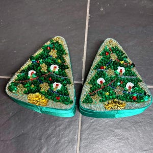 Op de afbeelding: Twee driehoekige doosjes met een ontwerp van een kerstboom van kralen en lovertjes. De bomen zijn groen met gouden, rode en witte accenten op een zilveren kralenachtergrond. De zijkanten van de doosjes zijn bekleed met groene satijnen stof.