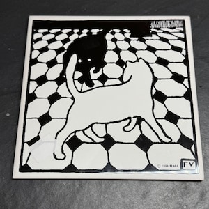 Puede incluir: Azulejo cerámico cuadrado con un diseño de gato en blanco y negro. La imagen presenta un gato blanco en primer plano y una silueta de gato negro en el fondo, sobre un patrón geométrico en blanco y negro. La baldosa está marcada con "© 1994 MMA FV".