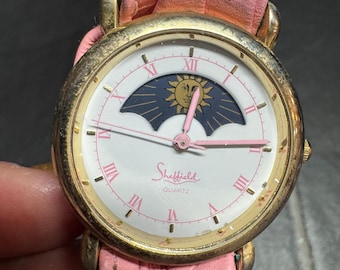 Reloj vintage Sheffield con fases lunares y sol, correa de piel rosa y movimiento de cuarzo dorado.