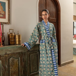 May include: A long-sleeved robe featuring a teal and green floral pattern with a blue and white striped trim along the collar, front opening, and sleeve cuffs. The garment includes a matching fabric tie belt at the waist.