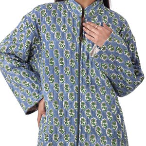May include: A light blue quilted jacket with a floral pattern in green and white. The jacket has a stand-up collar, a full-length zipper, and long sleeves. The jacket is approximately knee-length.