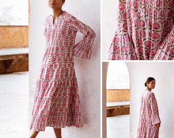 May include: A white dress with a pink floral print and a tiered skirt. The dress has long sleeves with bell cuffs and a V-neckline.
