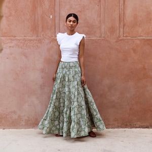 May include: A woman wearing a white ruffled top and a green floral maxi skirt with a smocked waistband.