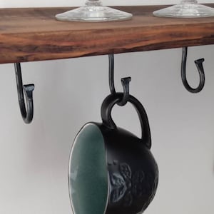 May include: A wooden shelf with black metal hooks. A green and black mug hangs from one of the hooks.