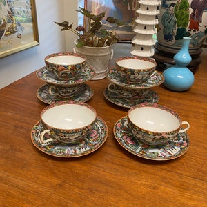 May include: Four porcelain teacups and saucers with a colorful floral and landscape design. The cups and saucers are white with a gold rim.