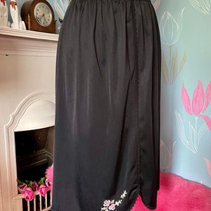 May include: Black slip skirt with a scalloped hem and embroidered floral design. The skirt is made of a silky material and has a side seam.