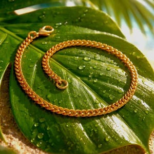 May include: A gold-toned chain bracelet featuring a classic curb link design. The bracelet is constructed with interlocking metal links and includes a secure lobster claw clasp at one end, providing a polished and uniform appearance throughout the piece.