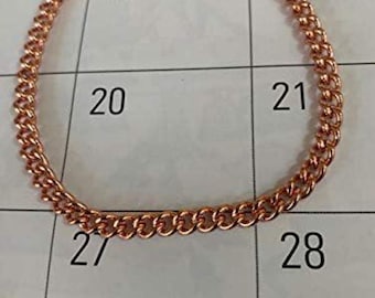May include: A copper-colored chain bracelet with a lobster clasp. The bracelet is made of small, interconnected links. The bracelet is resting on a calendar with the numbers 6, 13, 20, 21, 27, and 28 visible.