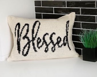 Peut inclure: Un oreiller en crochet blanc avec le mot "Blessed" en lettres noires.