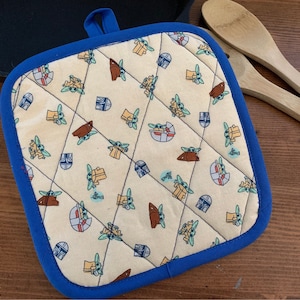 May include: A blue and white quilted pot holder with a repeating pattern of a green alien character and a spaceship.