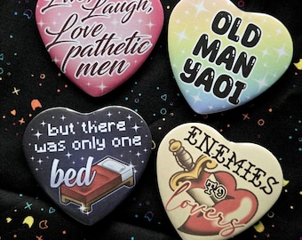 May include: Four heart-shaped buttons with humorous text. One button reads "Live, Laugh, Love pathetic men." Another says "Old Man Yaoi." The third says "but there was only one bed." The last says "Enemies to Lovers."