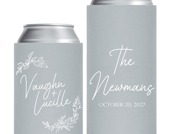 May include: Two light gray foam can coolers with white printed text. The shorter cooler features the names Vaughn + Lucille with floral accents. The taller slim cooler displays the text The Newmans and the date OCTOBER 20, 2027 in white lettering.