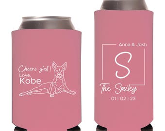 May include: Two pink foam can coolers with white text and graphics. The left cooler features a dog illustration with the text Cheers y'all! Love, Kobe. The right cooler displays a square frame, the letter S, Anna & Josh, The Smiley, and 01 | 02 | 23.