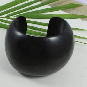 Könnte beinhalten: Ein breites, abgerundetes Armband in Schwarz. Das Armband besteht aus einem glatten, polierten Material.