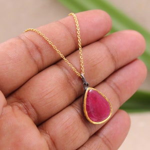 Può includere: Una collana con catena dorata con un ciondolo a forma di lacrima con una pietra preziosa rosa incastonata in una cornice d'argento con bordo dorato.