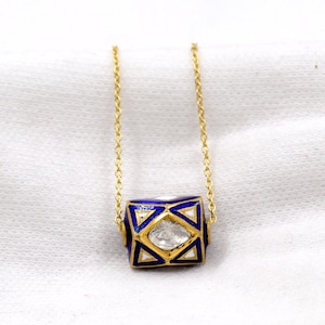 Puede incluir: Un collar de cadena de oro con un colgante de esmalte azul y blanco con un diseño geométrico y una piedra preciosa transparente en el centro.