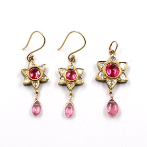 May include: A set of three gold earrings featuring pink and white gemstones. Each earring has a star-shaped design with a pink gemstone in the centre and white gemstones around the edges. The earrings are attached to a small pink teardrop-shaped gemstone.