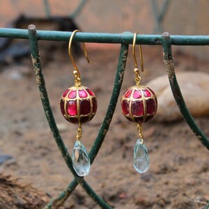 May include: Gold earrings with a red and gold sphere pendant and a teardrop-shaped blue gemstone dangle.
