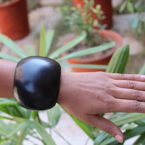Puede incluir: Un brazalete de madera negro con una superficie lisa y redondeada.