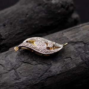 May include: A delicate gold and silver pendant featuring a leaf design with a single large diamond in the center and smaller diamonds surrounding it.