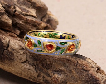May include: A gold ring with a blue enamel band and a floral design. The ring is set with three orange gemstones.