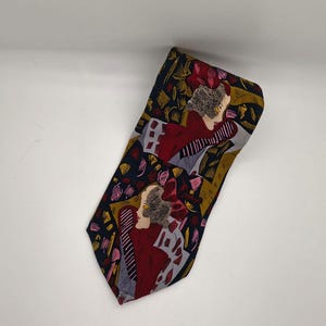 May include: A necktie featuring a dark navy blue background with a repeating graphic pattern of stylized figures in red, gold, and grey. The design includes abstract shapes and lines that create a layered, artistic composition across the fabric surface.