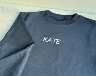 Puede incluir: Una sudadera azul oscuro con el nombre "KATE" bordado en blanco en la parte delantera.