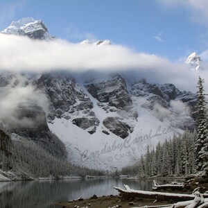 Puede incluir: Una cordillera nevada con un lago en primer plano. Las montañas están cubiertas de nieve y nubes. El lago está tranquilo y refleja las montañas. La imagen está tomada desde un ángulo bajo, mirando hacia las montañas.