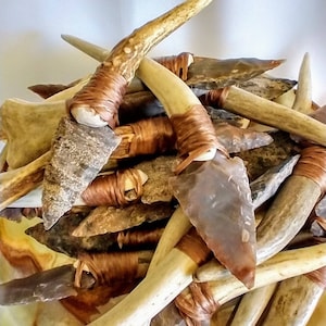 May include: A collection of arrowheads made from flint and antler, wrapped with copper wire. The arrowheads are various shapes and sizes, and the antler is a natural brown color.
