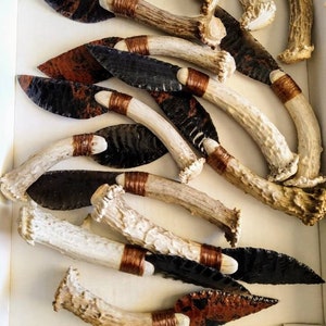 May include: A collection of handmade knives with black and brown obsidian blades and antler handles. The blades are wrapped with copper wire at the base of the handle.