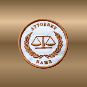 May include: Embroidered patch with a white center and a brown border. The patch features the word "ATTORNEY" at the top and "NAME" at the bottom. A scale of justice is in the center, surrounded by a laurel wreath.