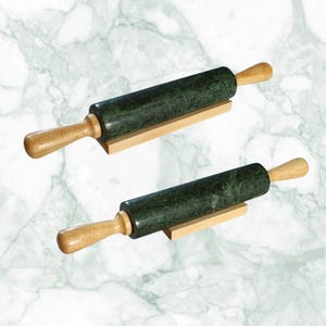 May include: Two rolling pins featuring dark green marble cylinders and light brown wooden handles. Each rolling pin is positioned on a small, rectangular wooden stand that supports the central marble barrel, keeping it elevated and stable.