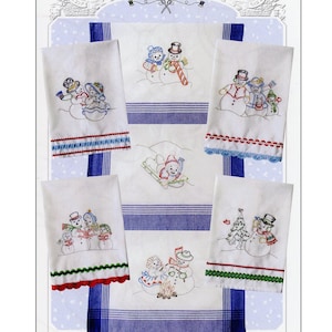 May include: A set of six white kitchen towels with embroidered snowmen designs. The towels feature various snowman scenes, including snowmen building a snowman, snowmen playing with a sled, and snowmen decorating a Christmas tree. The text "Snow Fun Towels" and "Iron-on Embroidery Transfer Included" is printed at the bottom of the image.