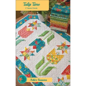 May include: A quilted table runner with a tulip design. The runner features colourful tulips and star patterns on a white background. The text "Tulip Time" and "5" Square Friendly" are visible.