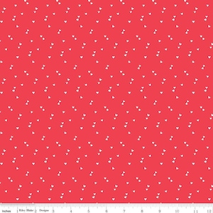 May include: Red fabric with a pattern of small white hearts scattered across the surface. The fabric has a ruler along the bottom edge, marked in inches. The text "Riley Blake Designs" is also visible.