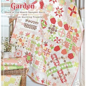 May include: A quilt titled Strawberry Garden Block of the Month Sampler Quilt and Companion Quilting Projects by Joanna Figueroa of Fig Tree Quilts. The quilt features a white background with red, green, and pink strawberry and star patterns.