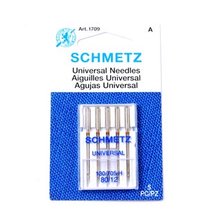 May include: A package of 5 Schmetz Universal sewing machine needles in a clear plastic case. The needles are silver and have a red band near the top. The package is blue and white and has the text "Art. 1709", "SCHMETZ", "Universal Needles", "Aiguilles Universal", "Agujas Universal", "SCHMETZ", "UNIVERSAL", "130/705 H", "80/12", "5 PC/PZ".
