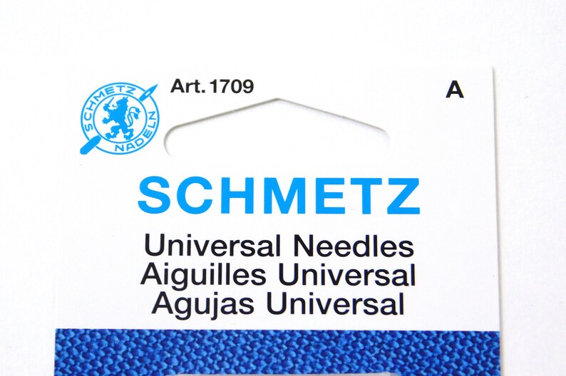 May include: A white package with blue text that reads "SCHMETZ Universal Needles Aiguilles Universal Agujas Universal" and a blue logo with a lion and the text "SCHMETZ NADELN" with the article number "Art. 1709" printed on the top. The package has a hole at the top for hanging.