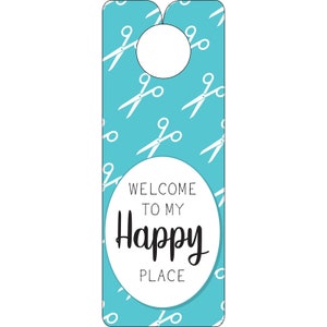 Peut inclure: Un porte-manteau turquoise bleu avec un cercle blanc au centre qui dit "Bienvenue dans mon lieu heureux". L'arrière-plan est recouvert d'un motif de ciseaux blancs.