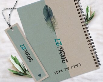 Peut inclure: Un agenda à reliure spirale et un marque-page assorti présentant un design divisé en vert sauge et beige. La couverture affiche une illustration de plume à l'aquarelle, le texte 2026|27 et des caractères hébreux. Le marque-page inclut un petit cœur.