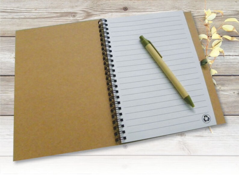 May include: A brown notebook with a white lined page and a green pen. The notebook has a black spiral binding and a recycle symbol on the cover.
