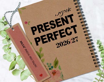 Peut inclure: Un carnet à spirales avec une couverture en papier kraft brun portant le texte PRESENT PERFECT 2026|27 et des illustrations florales. Un marque-page rectangulaire brun avec du texte hébreu et un petit cœur rouge est attaché par une ficelle bicolore.