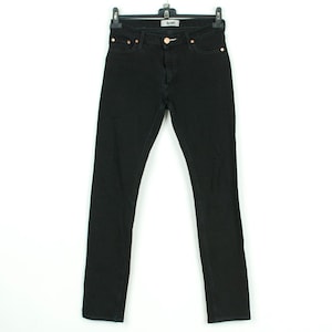 May include: Black denim jeans hanging on a black hanger. The jeans have a classic five-pocket design with copper-colored rivets and a button closure. The brand name "Acne" is visible on the button. The jeans are a straight-leg style.